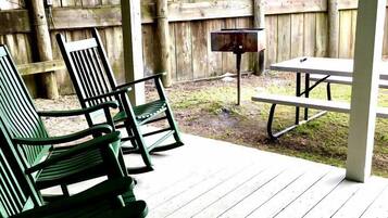 Une terrasse en bois avec des chaises vertes et une table de pique-nique, le tout entouré d’une clôture en bois.