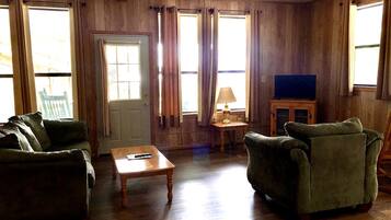 A room with wooden walls, a green sofa, a wooden coffee table, and a television on a cabinet.