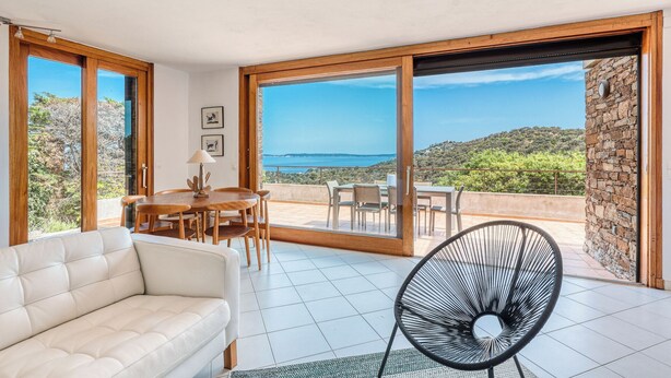 Ein modernes Wohnzimmer mit Sofa, Esstisch, Stühlen und einer großen Glasschiebetür, die auf einen Balkon mit schöner Aussicht führt.