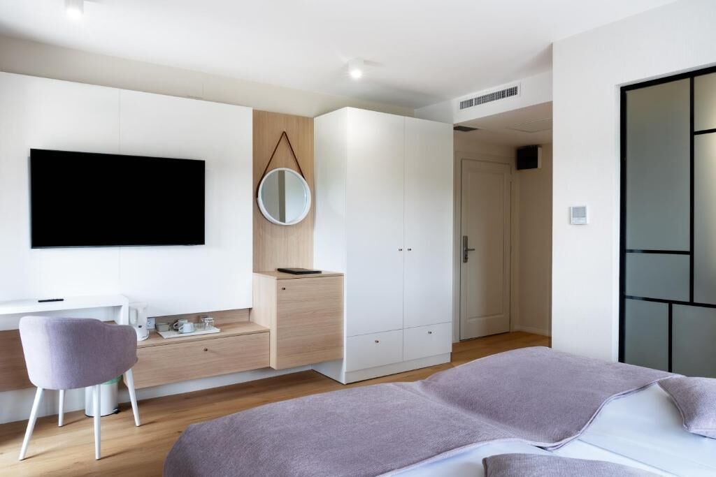 A modern bedroom with a bed, a desk, a chair, a wardrobe, and a TV mounted on the wall.