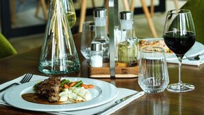 Una mesa de comedor con un plato de comida, una copa de vino y un florero con flores secas.
