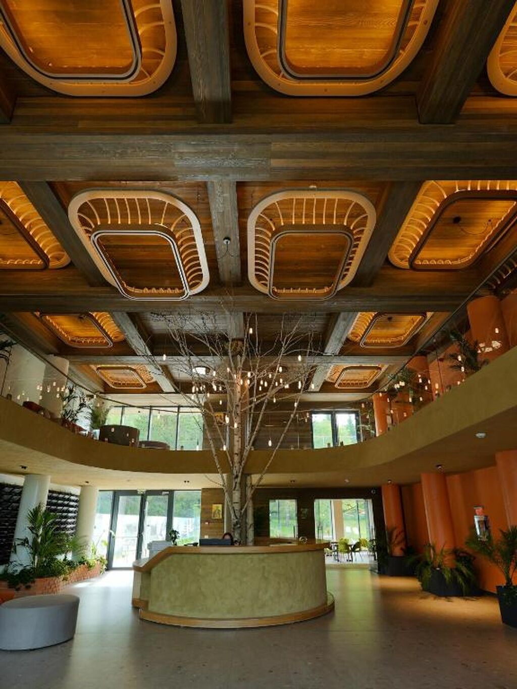 A spacious lobby with a central reception desk, large windows, and a high ceiling with exposed beams and lighting fixtures.