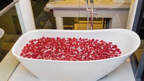 Eine weiße, freistehende Badewanne, gefüllt mit roten Rosenblüten.