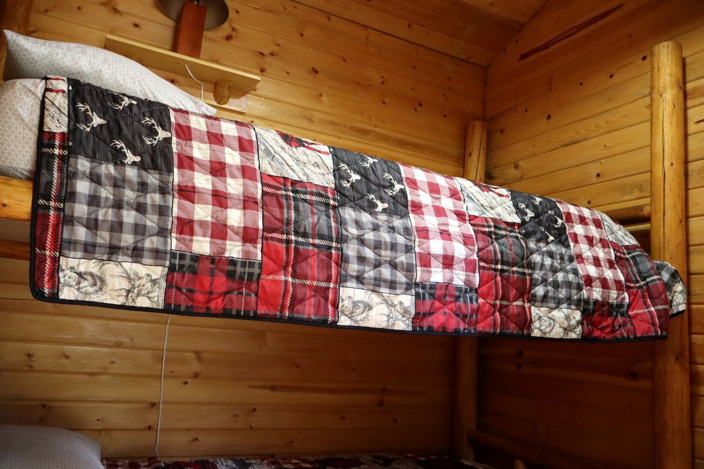 A wooden cabin interior with a quilted blanket hanging on the wall.