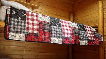 A wooden cabin interior with a quilted blanket hanging on the wall.