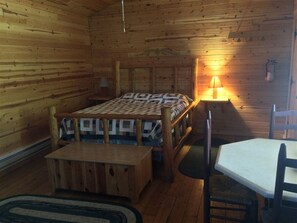 A wooden cabin room with a bed, a table, and a chair.