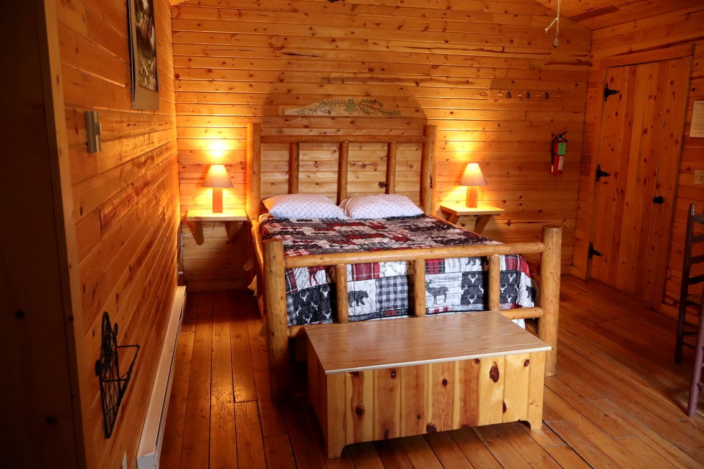 A wooden cabin room with a bed, two bedside tables, a bench, and a door.