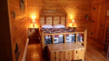 A wooden cabin room with a bed, two bedside tables, a bench, and a door.