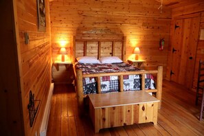 A wooden cabin room with a bed, two bedside tables, a bench, and a door. - Family-Friendly Vacation Rental for Four near Missoula, Montana (Hall)