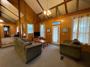 A spacious living room with wooden walls, a sofa, a coffee table, and a television. - Charming Family Cabin with Private Pond and Fire Pit near Zwolle, Louisiana (Zwolle)
