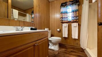 Ein Badezimmer mit Holzwandverkleidung, Waschbecken, Toilette und Duschvorhang.