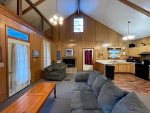 A spacious living area with a fireplace, wooden walls, and a kitchen with wooden cabinets. - Charming Family Cabin with Private Pond and Fire Pit near Zwolle, Louisiana (Zwolle)