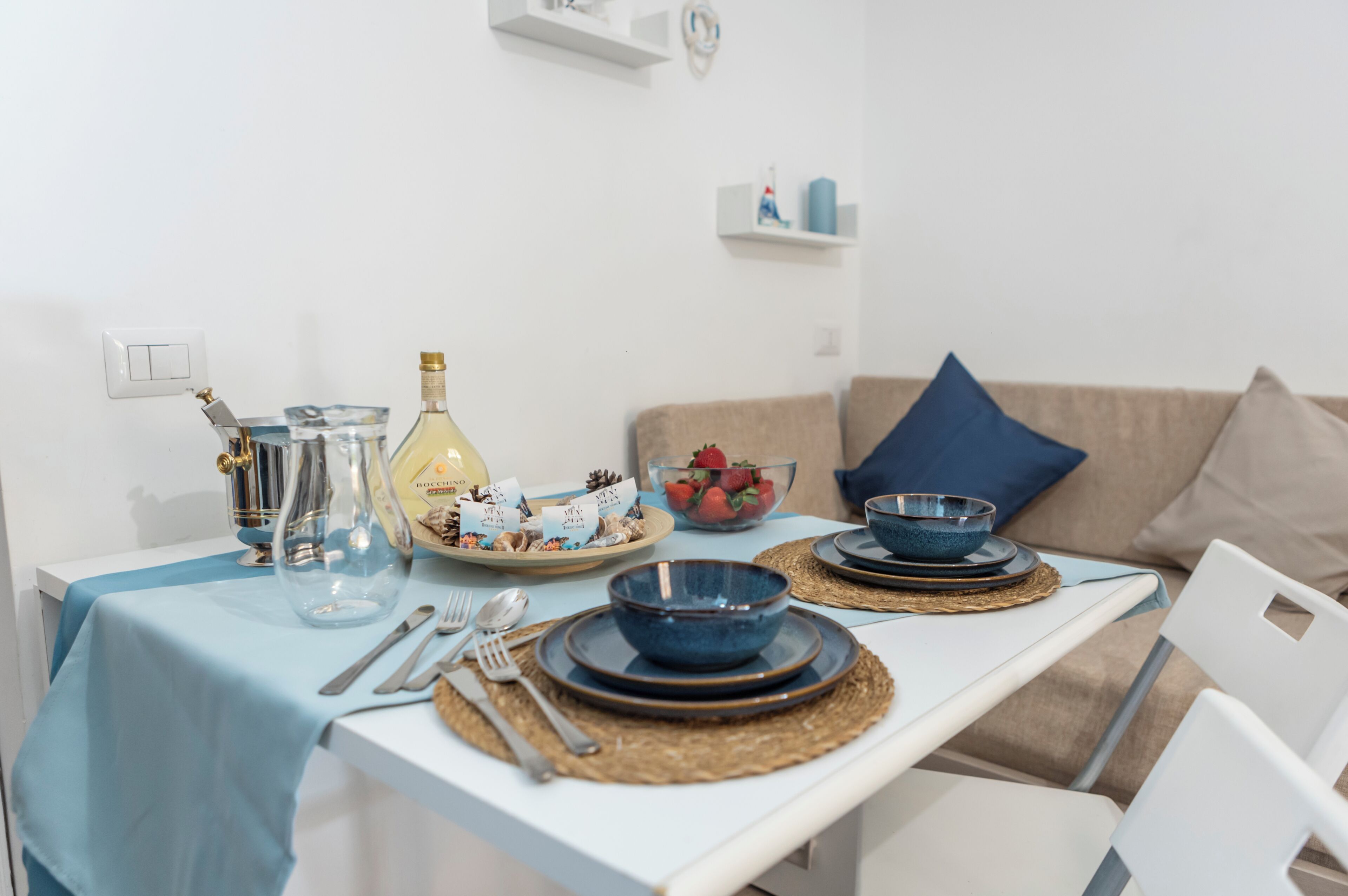 A dining table set with blue plates, bowls, and cutlery, a bottle, and a bowl of strawberries.