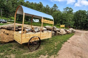 Ein hölzerner Wagen mit einem blauen Vordach, auf dem 'Fiftywood $7 Cash In Box' steht, und mit Holzscheiten beladen.