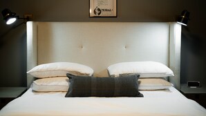 Un llit ben fet amb almoinades blanques i grises, un cartell al quadre sobre seguretat i moral, i dues làmpades de nit.