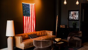 A room with a leather sofa, two armchairs, a lamp, a framed photo, and an American flag.