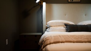 A bedroom with a bed, pillows, a bedside table, and a wall socket.