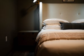A bedroom with a bed, pillows, a bedside table, and a wall socket.