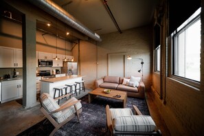 A modern kitchen with white cabinets, a central island with stools, a sofa, and a coffee table. - The Shumaker | Unit 101 | Modern Lancaster Apt (Lancaster)