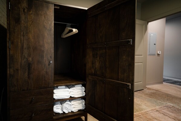 A wooden wardrobe with shelves and hanging space, a door, and a carpeted floor. - The Shumaker | Unit 101 | Modern Lancaster Apt (Lancaster)