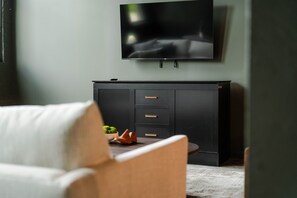 A modern living room with a flat-screen TV mounted on the wall, a dark wooden cabinet with drawers, and a white sofa. - The Shumaker | Unit 107 | Chic Lancaster Apt (Lancaster)