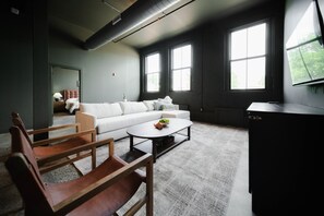 A modern room with a white sofa, wooden chairs, a coffee table, and large windows. - The Shumaker | Unit 107 | Chic Lancaster Apt (Lancaster)