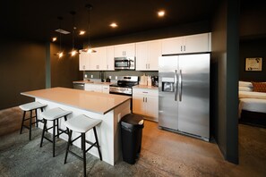 A modern kitchen with white cabinets, stainless steel appliances, a central island with bar stools, and pendant lighting.