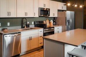 A modern kitchen with stainless steel appliances, light-colored cabinets, and a central island. - The Shumaker | Unit 107 | Chic Lancaster Apt (Lancaster)
