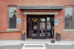 A brick building with a sign reading 'The Shumaker' and a 'Leasing Office' sign above the entrance. There are two parking signs indicating reserved parking for disabled individuals. - The Shumaker | Unit 107 | Chic Lancaster Apt (Lancaster)