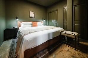 A bedroom with a bed, bedside lamps, a nightstand, a bench, and a door.