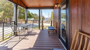 Een houten terras met een tafel en stoelen, een glazen deur en uitzicht op een straat en gebouwen.