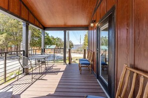 A wooden deck with a table and chairs, a glass door, and a view of a street and buildings. - Rustic Cabin Retreat with Loft, Fire Pit & Community Pool in Branson, Missouri (Branson)