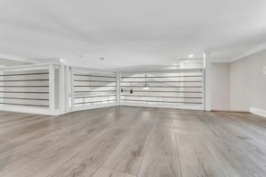 Una habitación amplia con piso de madera, paredes blancas y un gran ventanal.