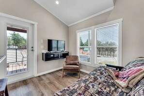 Ein Schlafzimmer mit Bett, Stuhl, Wand-Fernseher und Balkon.