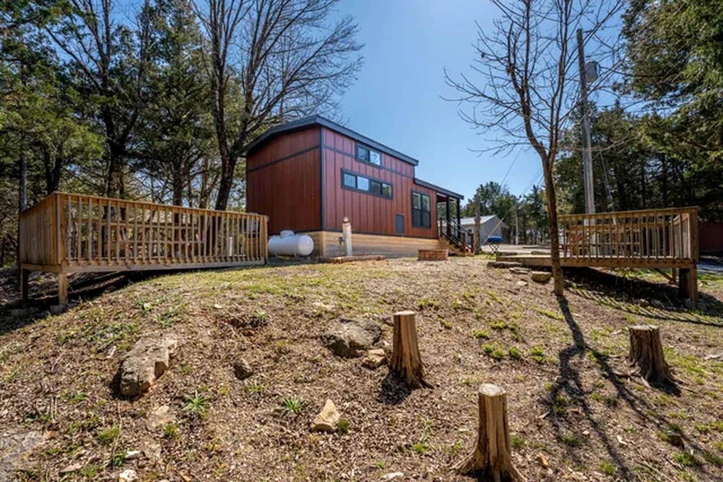 A modern building with a red exterior, surrounded by a natural landscape with trees and a wooden bridge.