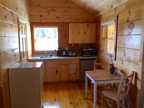 A compact kitchen with wooden cabinets, a refrigerator, a microwave, and a dining table with chairs.