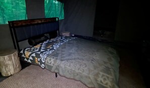 A bed with a patterned bedspread, a wooden headboard, a small round stool, and a tree stump.
