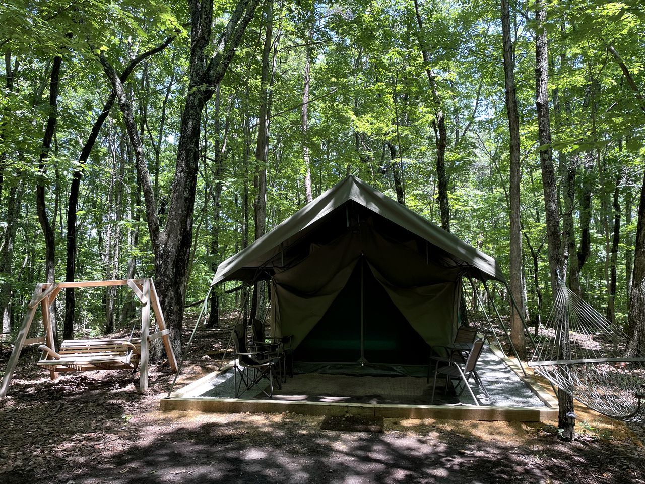 A tent set up in a forest with a hammock and a swing.