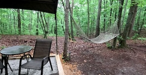 A hammock in a forest, a table with chairs, and a covered area.