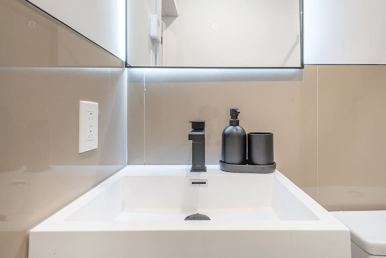 Een moderne badkamer met een witte wastafel, een zwarte kraan en twee zwarte bakjes op het aanrecht.