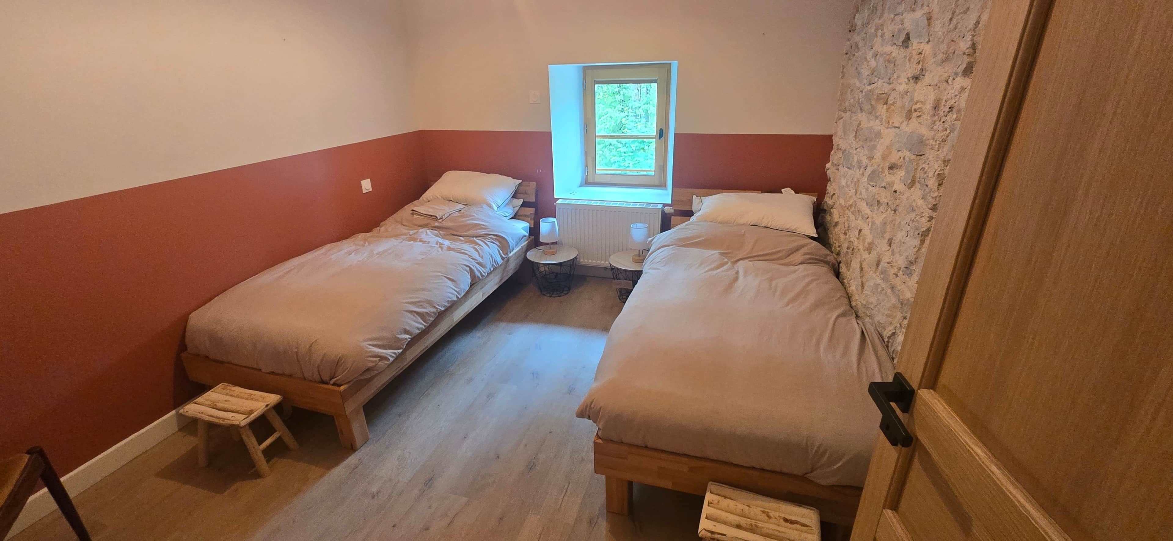 Une petite chambre, de taille modeste, comprenant deux lits simples, une petite table et une fenêtre laissant entrer la lumière naturelle.
