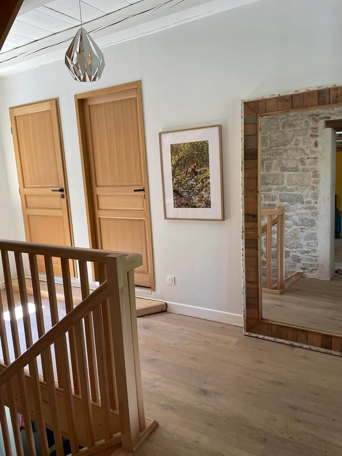 Una stanza con porte in legno, un quadro incorniciato appeso al muro, un muro in pietra e una scala di legno.