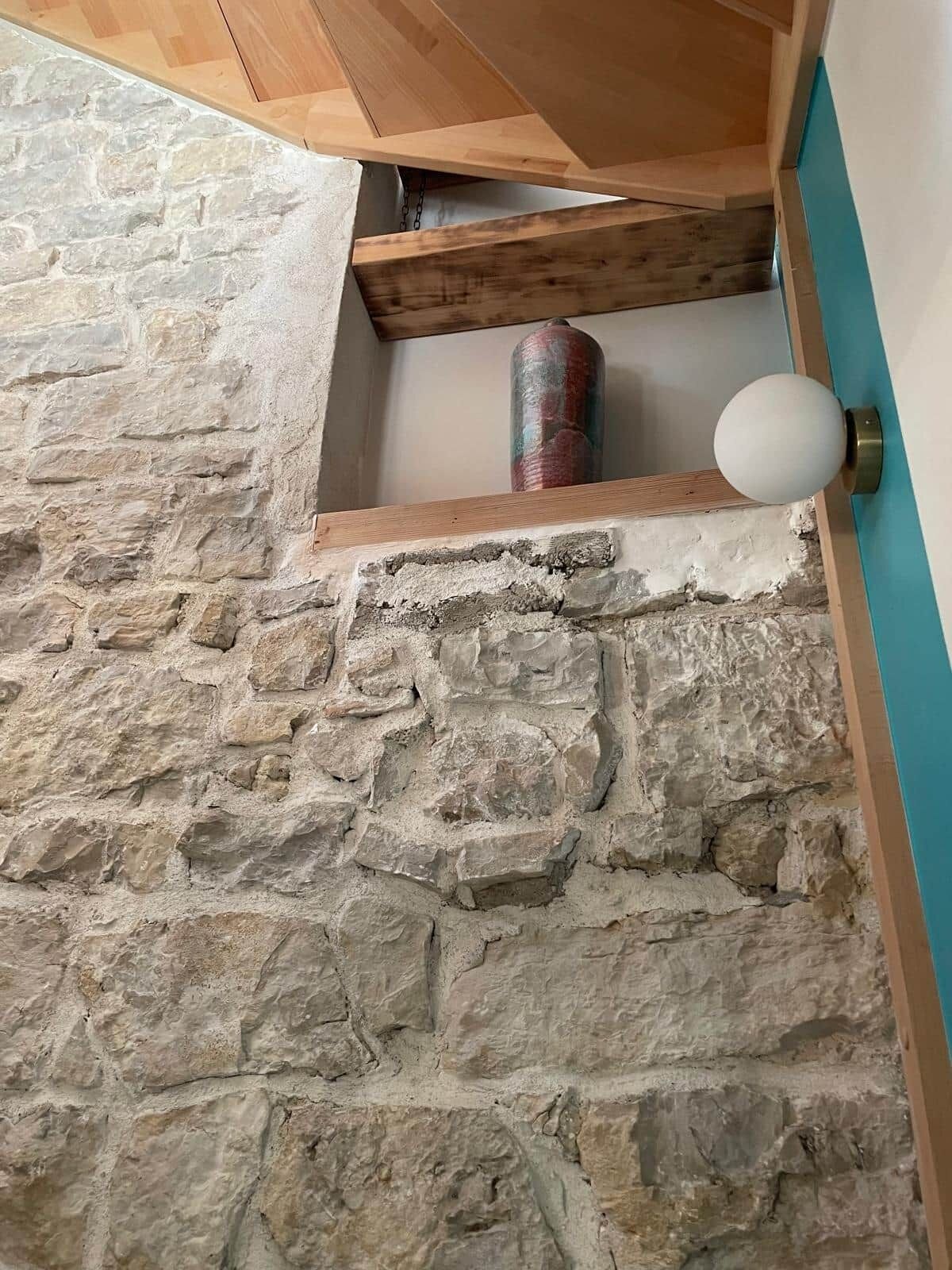 A stone wall with a wooden shelf and a cylindrical object.