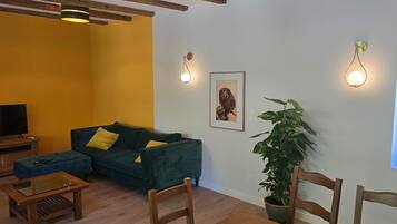 Uma sala de estar com sofá, televisão, mesa de centro e um vaso de planta.