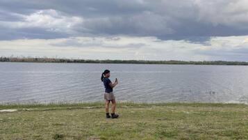 A person standing by a lake with a grassy foreground and a cloudy sky.