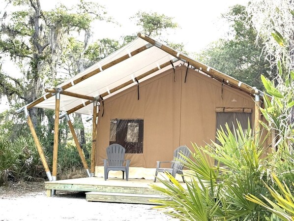 A tent with a wooden frame and a canvas roof, two chairs, and a small table in front.
