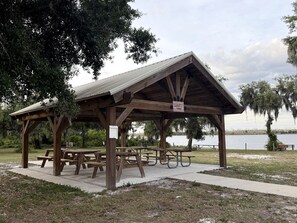 A wooden pavilion with picnic tables, a sign indicating it is a rest area, and a body of water in the background.