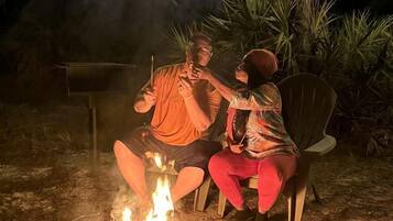 Two people sitting on chairs around a campfire at night.