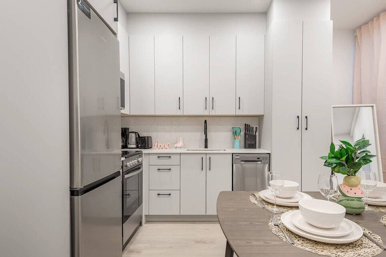 A modern kitchen with white cabinets, stainless steel appliances, and a dining area with a table set for four.