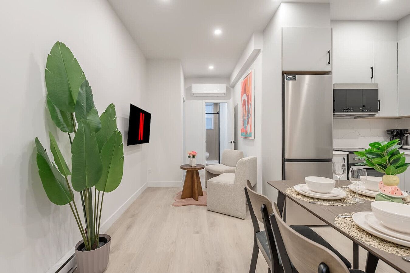 A modern kitchen with a built-in refrigerator, a dining area with a table and chairs, and a large potted plant.